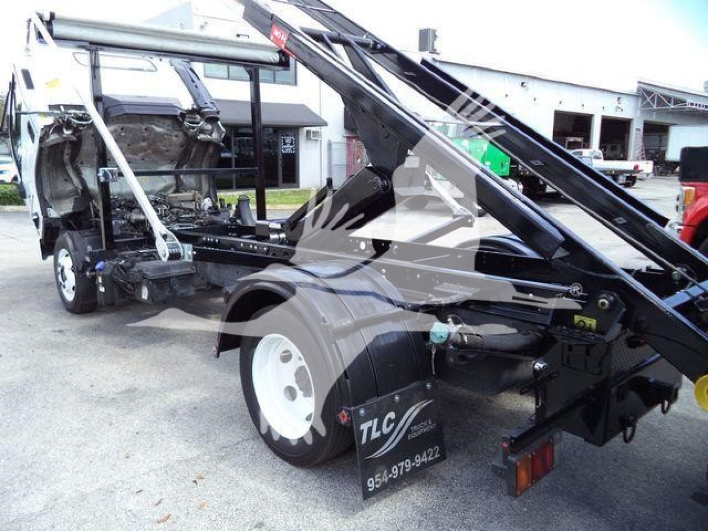 Isuzu NPR/RR truck chassis with roll-off hoist and wheel, side view showing hydraulic arms and TLC sticker on rear wheel area.