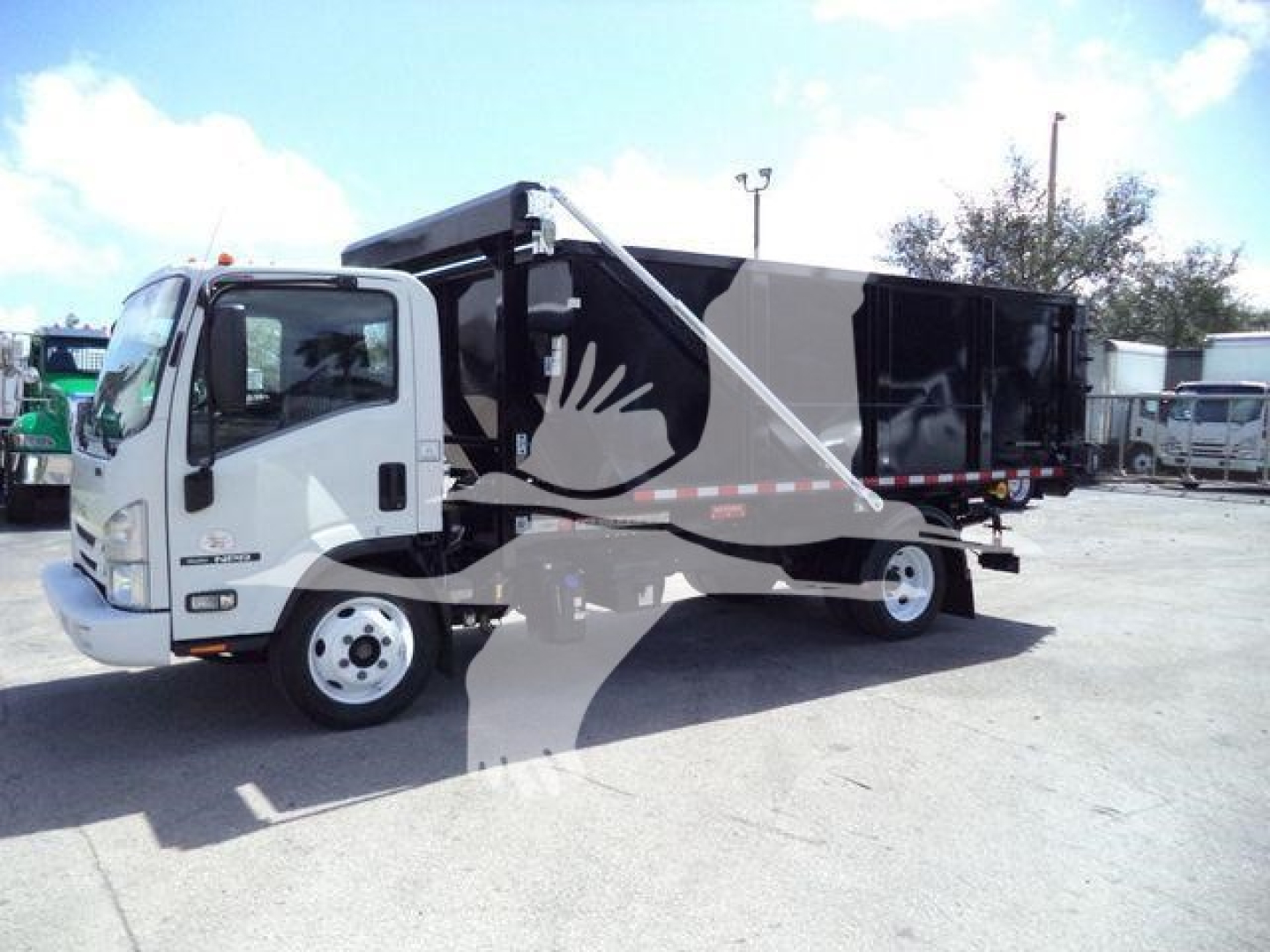 Isuzu NPR/NRR style roll-off truck with a gray/black dump body and hydraulic arm visible, parked in a lot.
