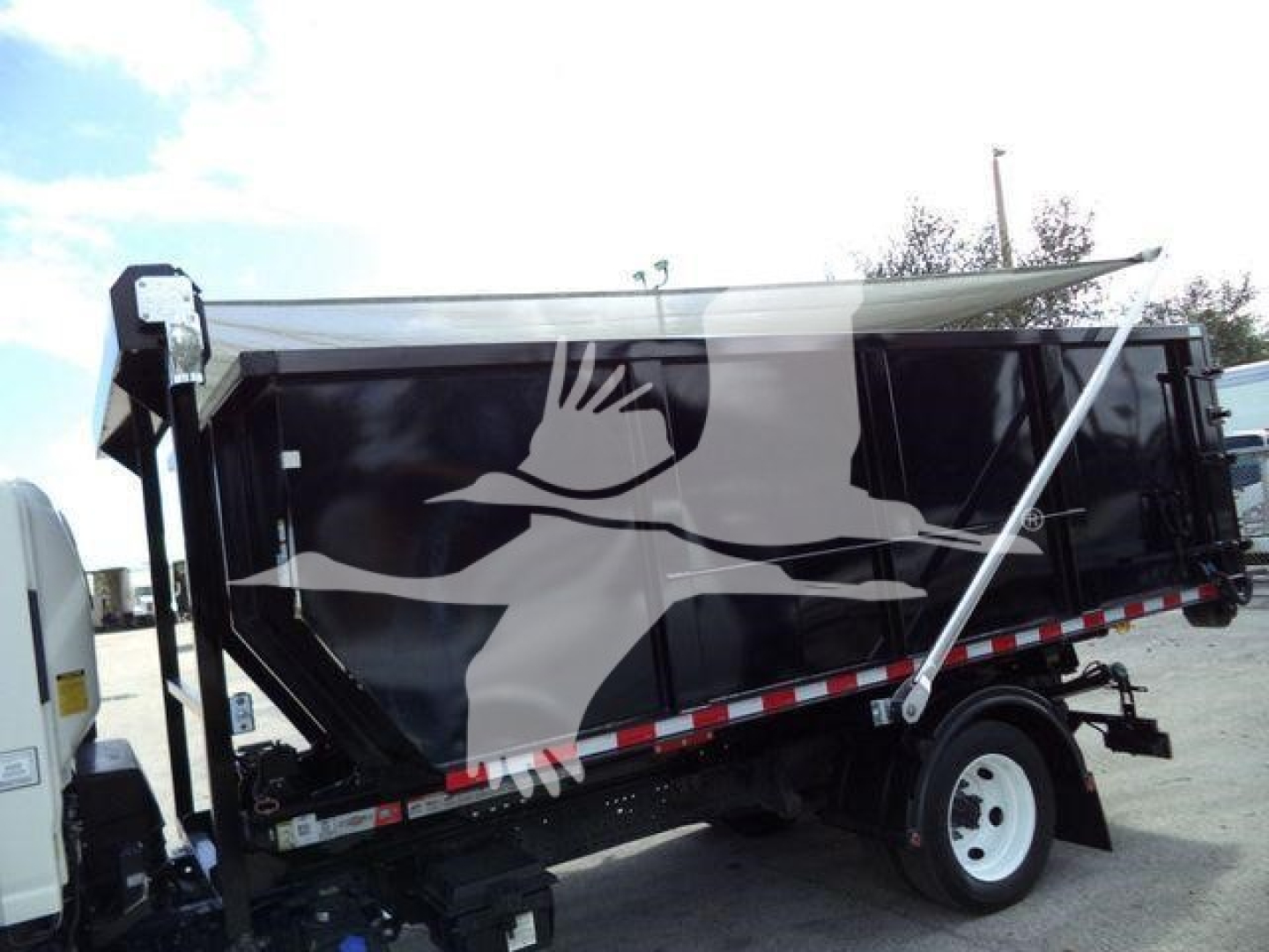 Isuzu NPR/NRR roll-off truck bed in side view showing graphic artwork and hydraulic hoist with tilted bed.
