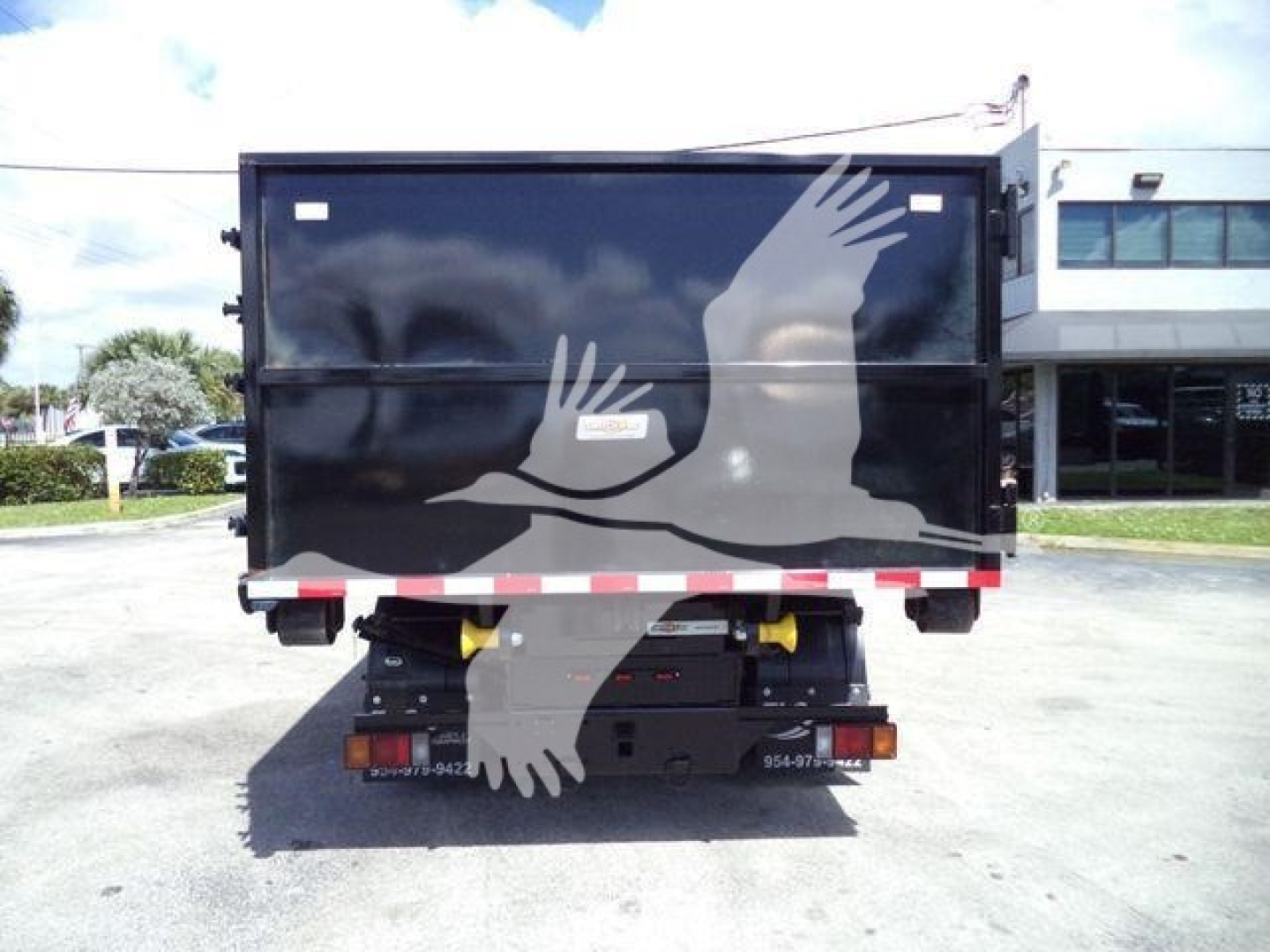 Isuzu NPRR roll-off truck rear view showing black cargo container with white dove graphic and taillights, bumper, and wheel arches visible.