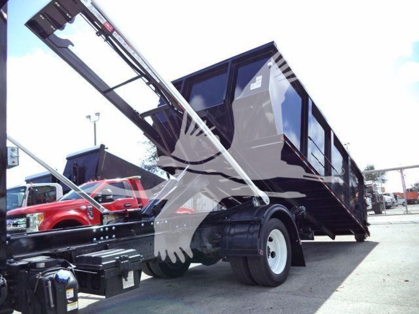Isuzu NPRR truck with a roll-off container attached, chassis facing left, hydraulic arm raised, black container bin in loading position.