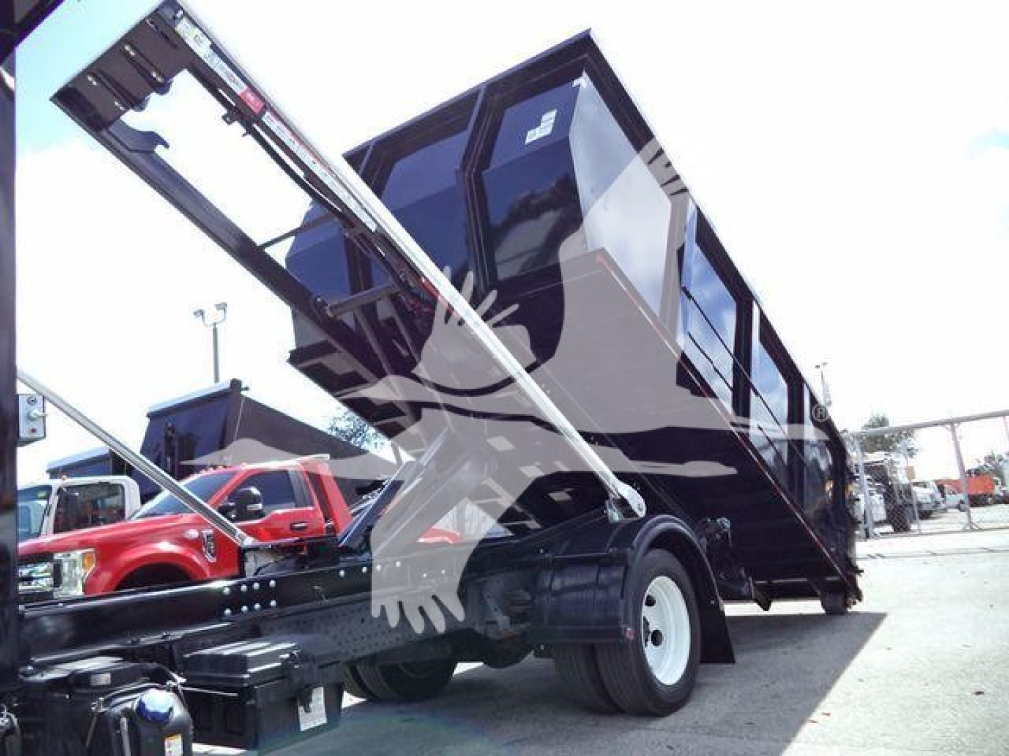 Isuzu NPRR/Rolloff truck with hydraulic lift and dump bed in service position showing black container and chassis.