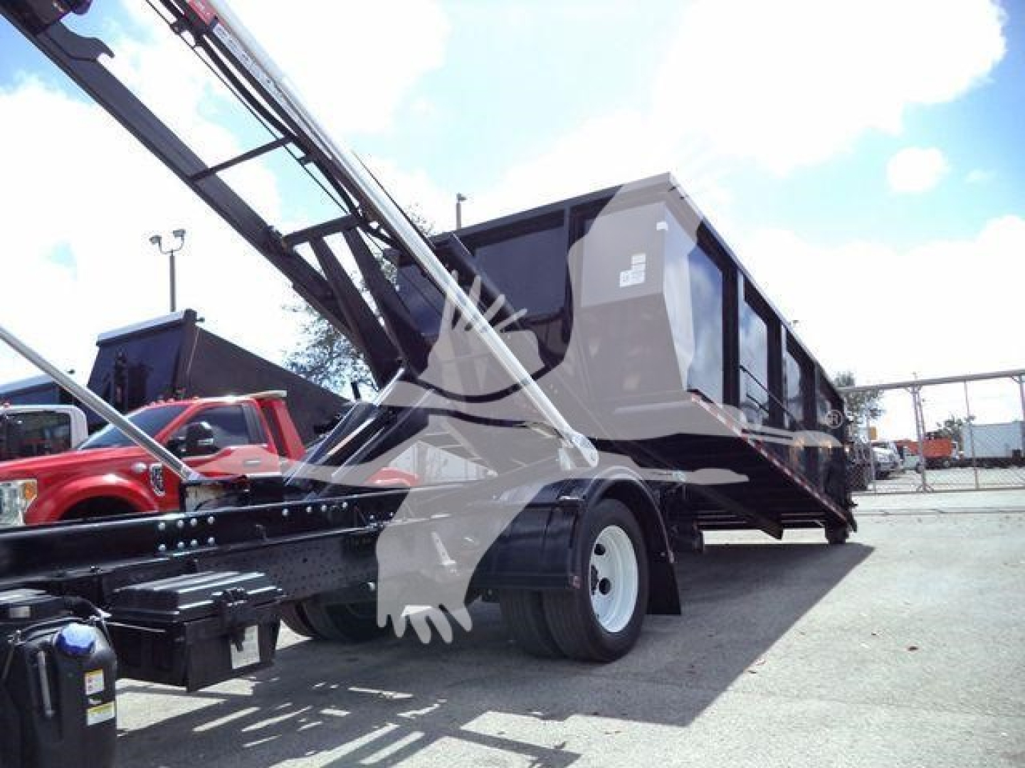 Rolloff truck trailer with hydraulic lift arm, large black container, and white wheels; visible but illegible text on side panels.