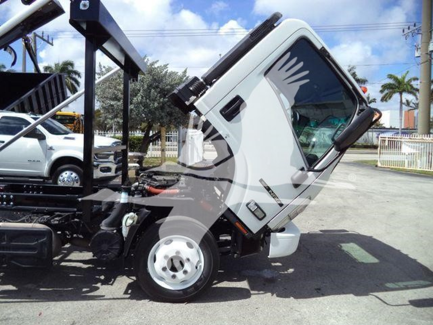 Isuzu NPR truck cab tilted, front showing cooling system and wheel with visible warning decals and hydraulic components in a yard.