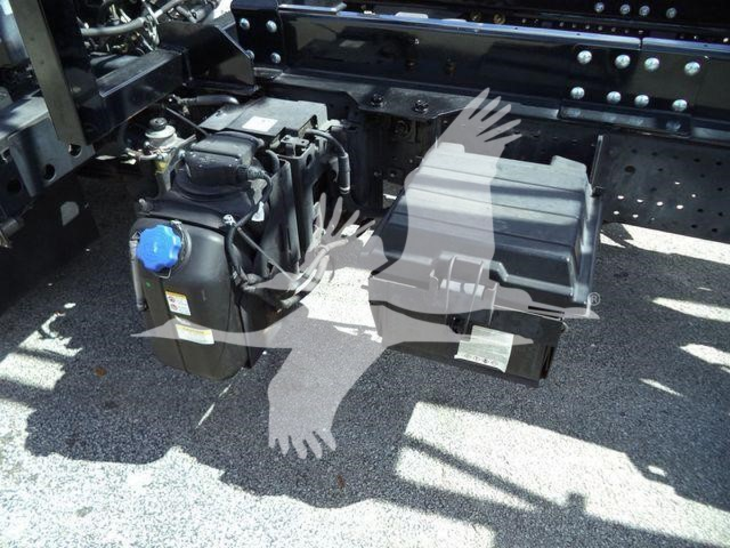 Isuzu NPR or NRR truck undercarriage showing battery box and auxiliary components with blue positive cap and black electrical enclosures.