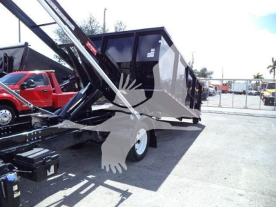 Isuzu NPR/NRR roll-off truck with a raised steel dump body attached to a hydraulic lift, side view showing rear wheel, cab in background, outdoor yard.