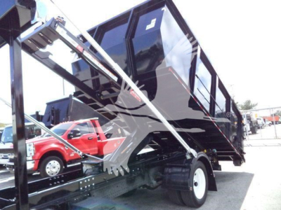 Isuzu NPR/Nrr roll-off truck in-service with hydraulic arms and tipped cargo bed, side view showing blue-black container and dual rear wheels.