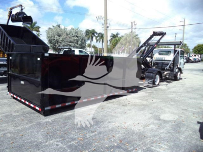 Isuzu NPR or similar roll-off truck with large black dumpster container and hydraulic hoist in a parking lot.