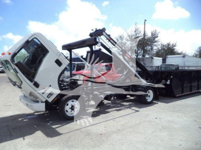 Isuzu NPR/NRR truck in roll-off configuration with tilted cab and hydraulic crane arm, white cab, black container, front left view.