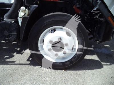 Isuzu NPRR wheel and tire assembly showing front left wheel with white hub, tire branding, and surrounding suspension components.