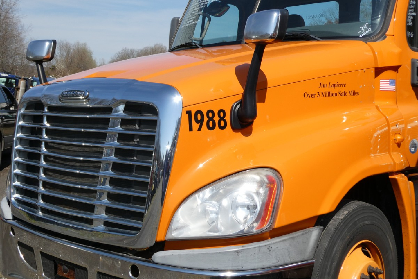 Truck hood showing Freightliner Cascadia 125 with orange paint, chrome grille, and number 1988 on fender.