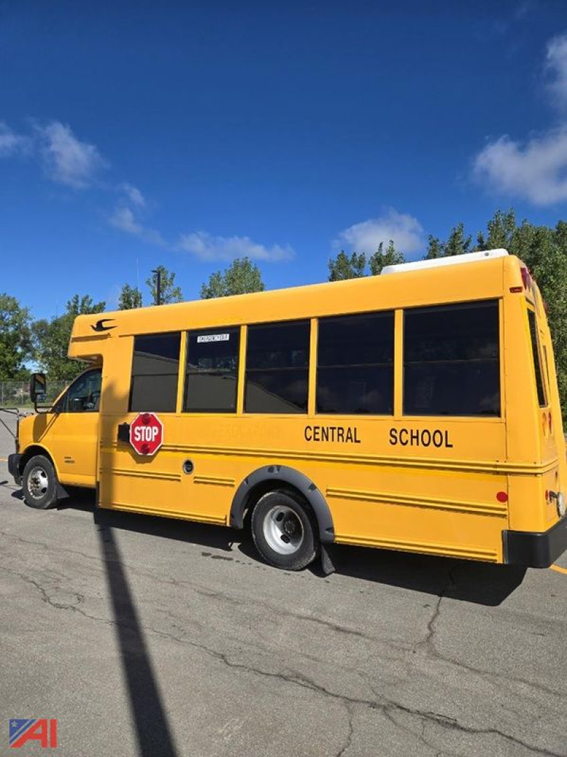 Yellow school bus with central school markings and stop sign, side view, blue sky.
