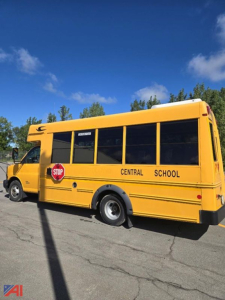 Yellow school bus with central school markings and stop sign, side view, blue sky.