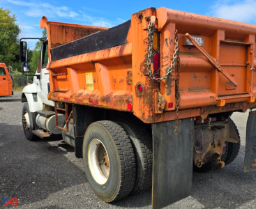 Dump truck bed of a 2003 International WorkStar 7300 with plow visible at rear, orange body, chain and mudflaps, side view of dual rear wheels.