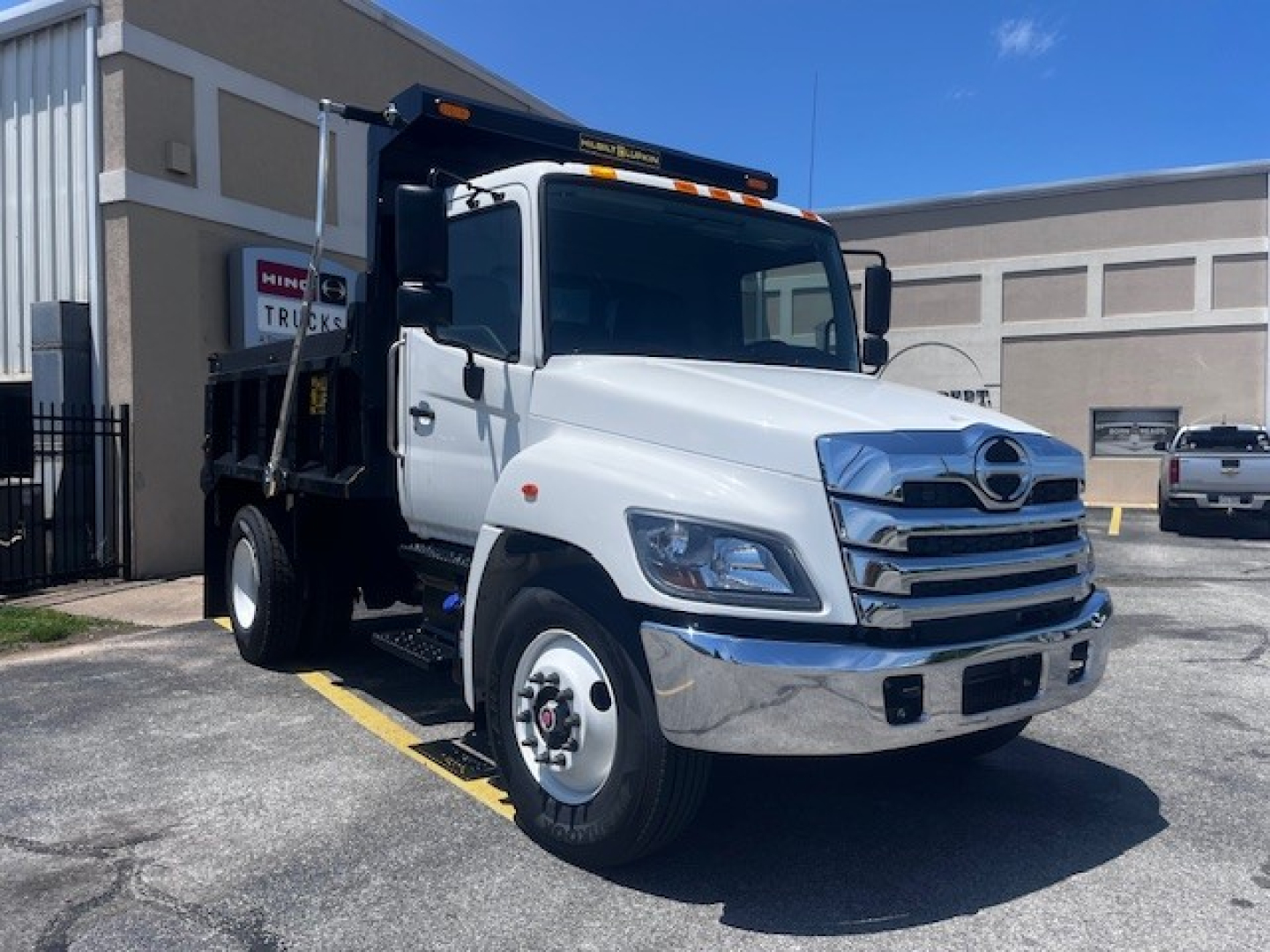 White 2026 Hino L7 dump truck in a parking lot showing front grille, headlights, and dump bed