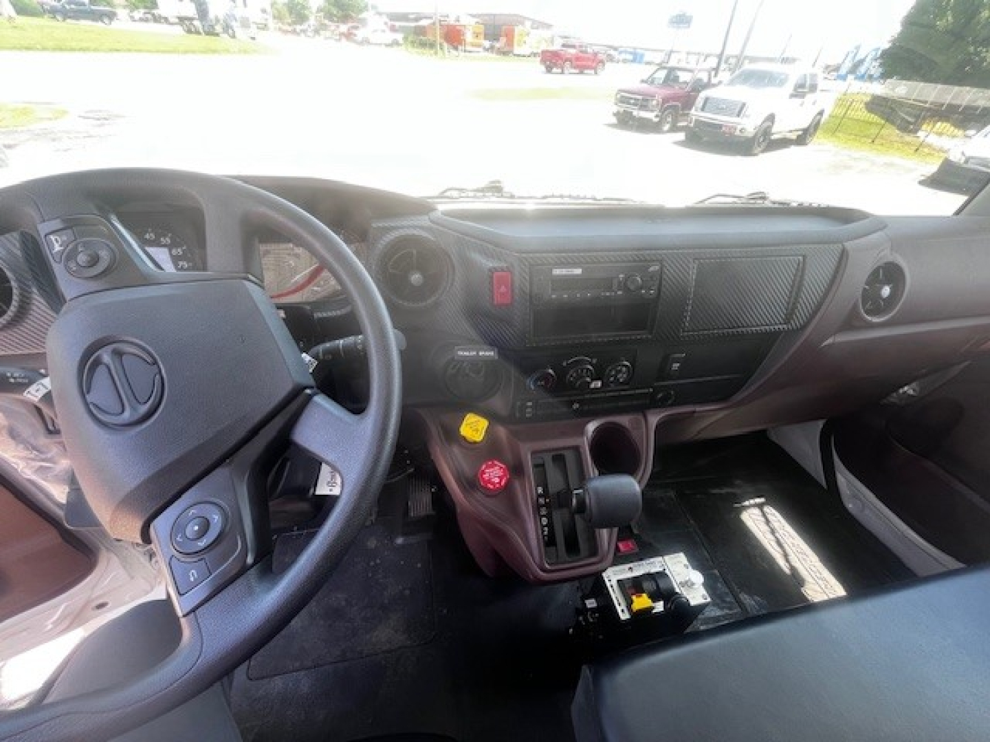 Front interior of a 2026 Hino L7 truck cab showing steering wheel with logo, dashboard, gear shifter, and control panels.