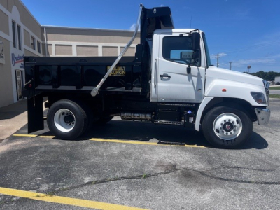 Truck bed with dump body on a white cab; side view shows hydraulic hoist, black dump box, white front wheel, and label visible on the box.