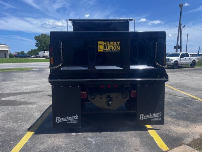 Dump truck bed showing the rear with Brackens mud flaps, Hilbilt Lufkin logo, and hitch area; black steel dump body with chain lifts and tailgate latches.