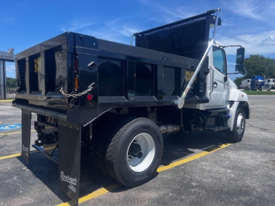 Hino dump truck rear and side view showing dump bed and wheel, with brand panels and safety chains.