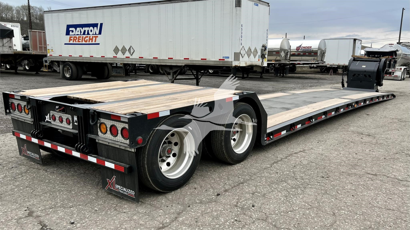 Trailer lowboy showing dual rear wheels and long flatbed with Daylight Freight trailer in background and dashboard lights; visible branding on rear mudflap and side rails.