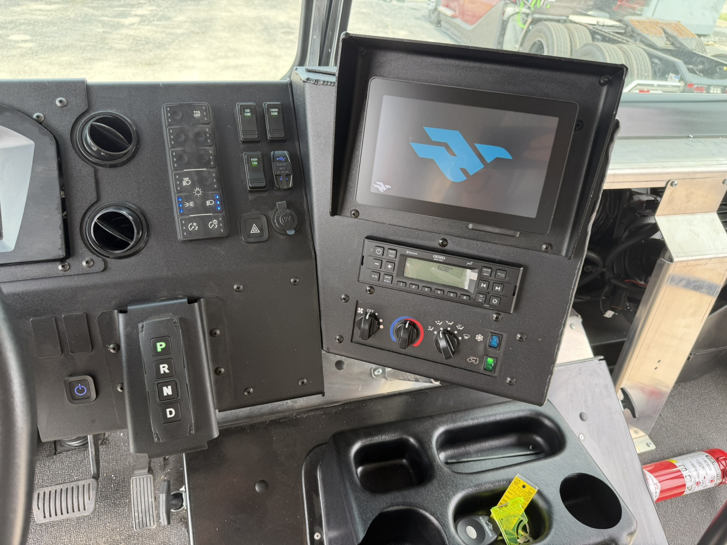 Harbinger S534 truck cabin dashboard with center-mounted display screen and control panel showing various switches and knobs, gear selector PRND, and cup holders.
