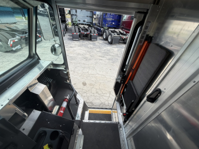 Harbinger S534 step van interior view from driver’s side doorway showing entry steps, floor mat, and stainless panels; control area with small compartments and fire extinguisher visible.