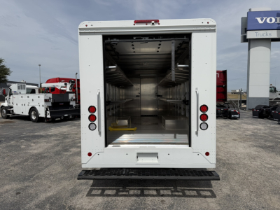Rear view of a white Harbinger S534 step van with an empty stainless steel interior and shelving on both sides.