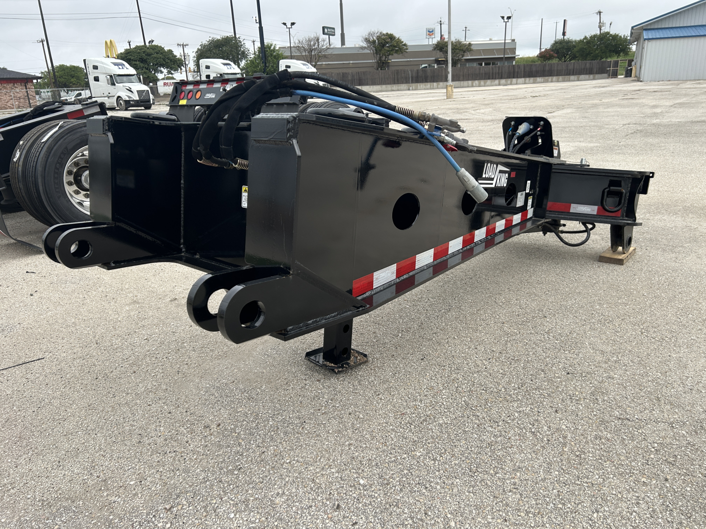Load King trailerSB141/2-43 coil trailer in black showing hydraulic lines and dual eye hitch, side rails, red white reflective tape, and support jack.