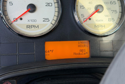 Dashboard gauges showing RPM and speedometer with orange digital display reading 19806 hours and ABS Module label; exterior of truck cab dash.