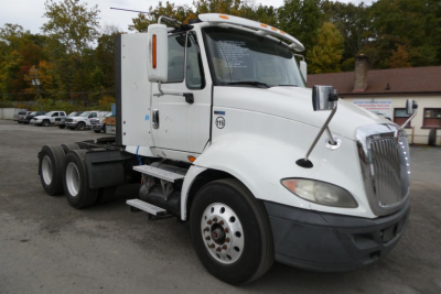 International ProStar+ 113 daycab truck in white, side view showing cab, front grille, and dual rear axles with stock number label on door.