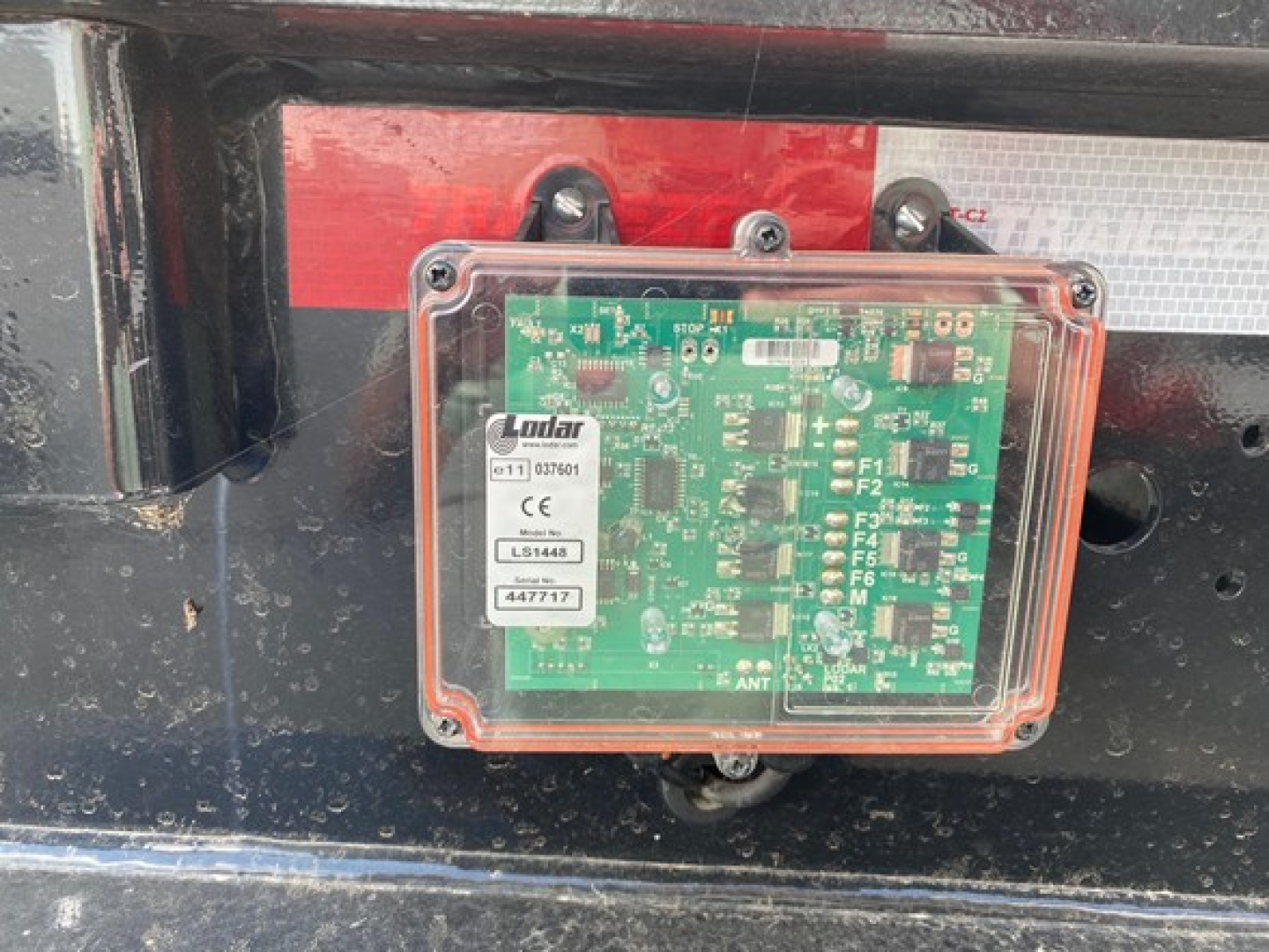 Trailer axle control module enclosure mounted on chassis with a green circuit board and connectors inside, label with barcode visible