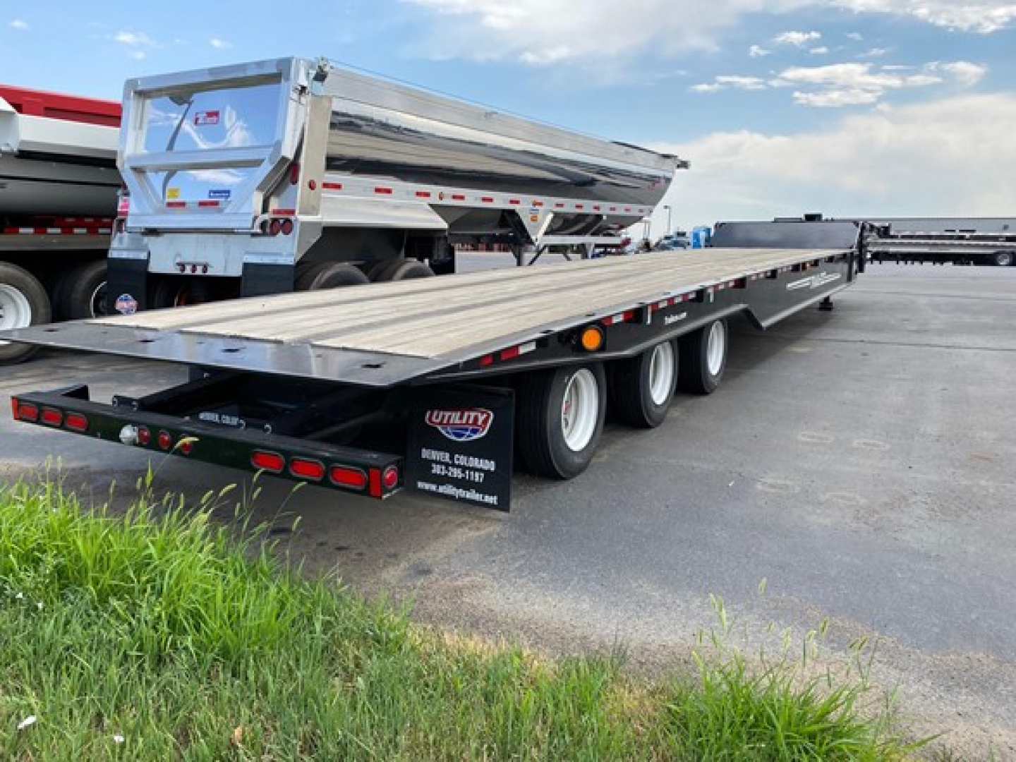 Trailer flatbed low-angle view showing long platform with triple-axle wheels and side markers, Trail-Eze branding visible on tail area.