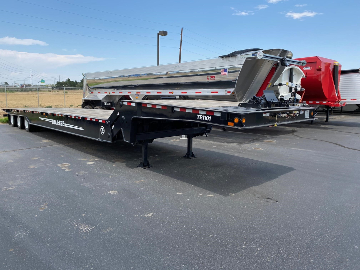 Trail-Eze TE1101 trailer with a lowered dump body, side view showing TE1101 model number and polished metal surface, black trailer deck, white and red reflective tape, parking lot.
