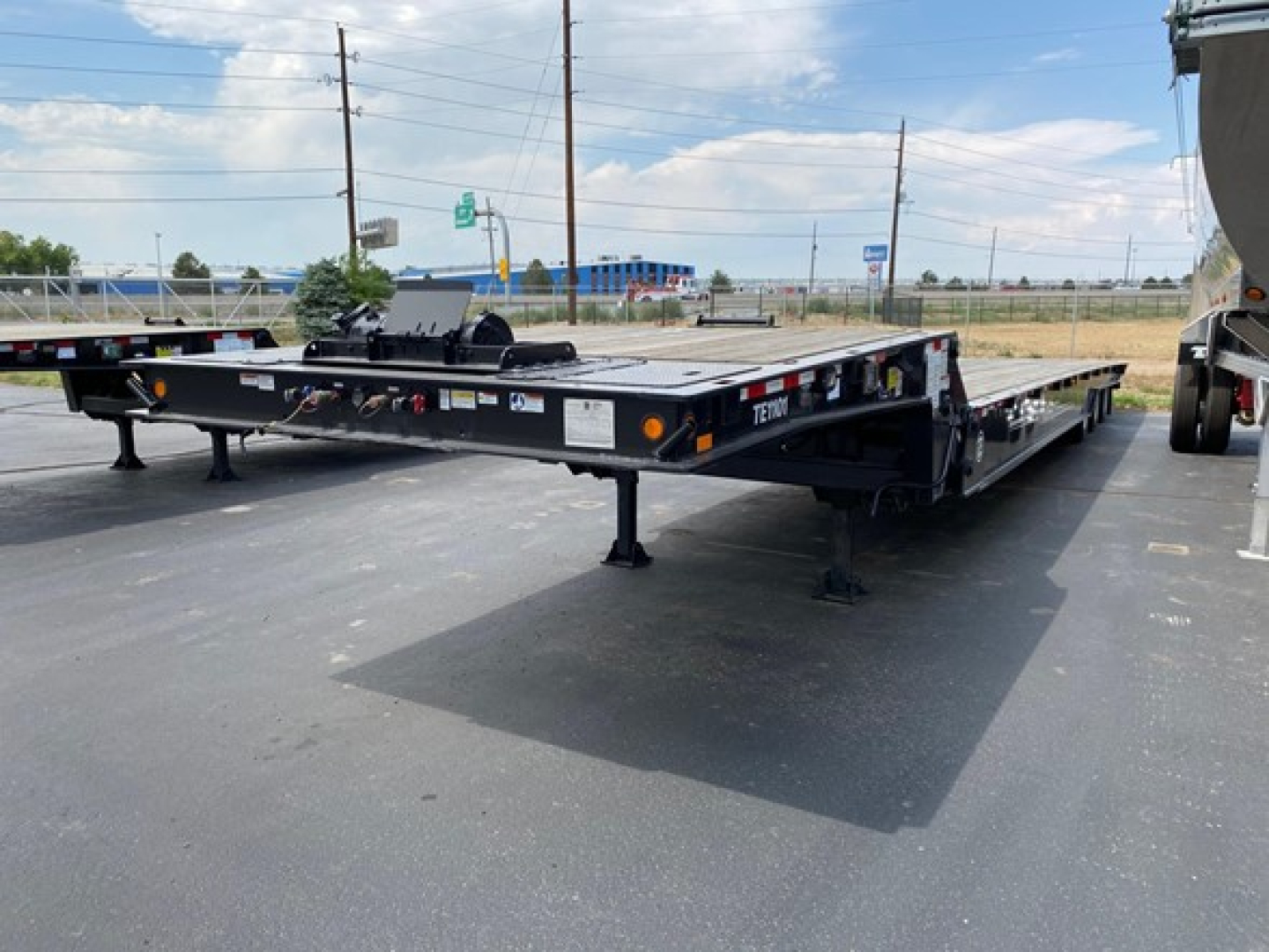 Trail-Eze TE1101 trailer deck showing multiple axles and adjustable landing gear, black frame with safety rails and tires visible.