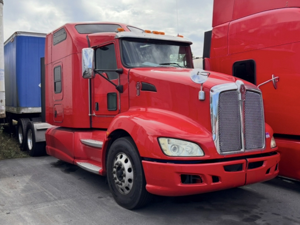 Kenworth T660 aero cab red semi truck in a lot, front-left view with chrome grille and sleeper cab.