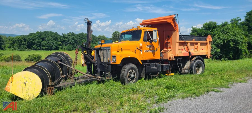 International dump truck with plow and wing attachment in field showing orange cab and dump bed