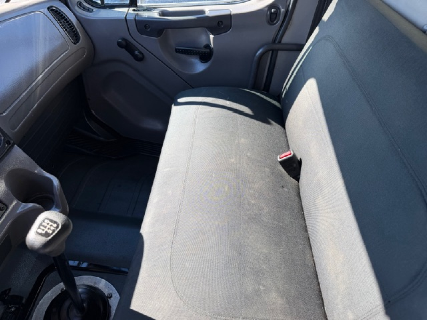 Truck cab interior showing front bench seat and gear shifter in Freightliner M2 106 cab, with transmission lever and door panel visible.