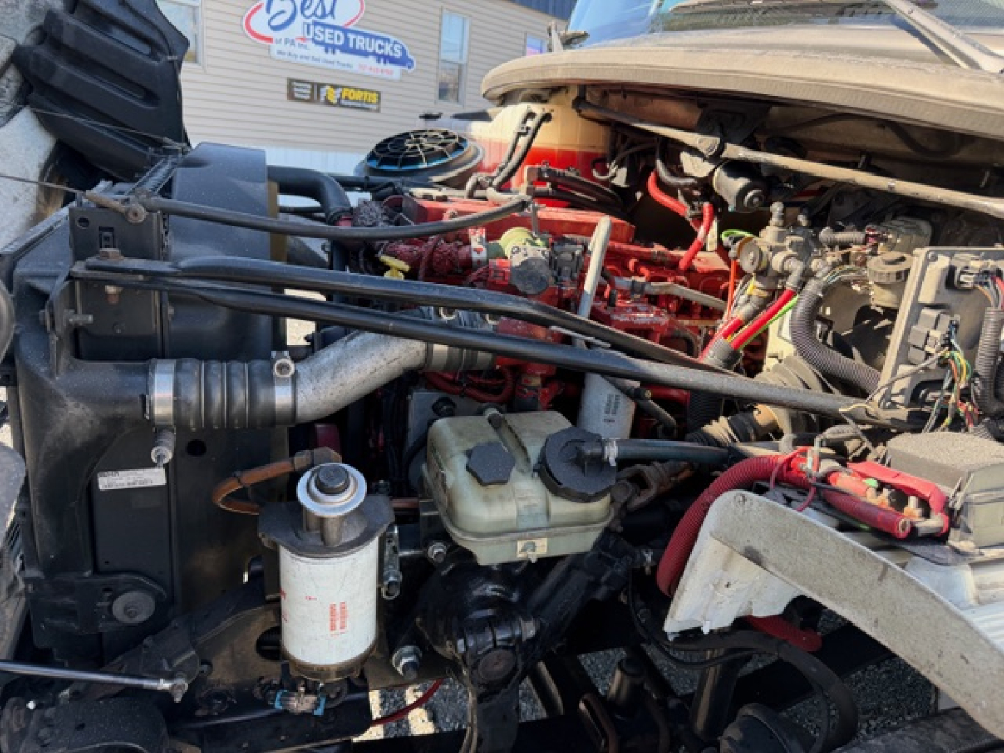 Freightliner M2 106 engine bay showing coolant reservoir, air intake, hoses, and label stickers.