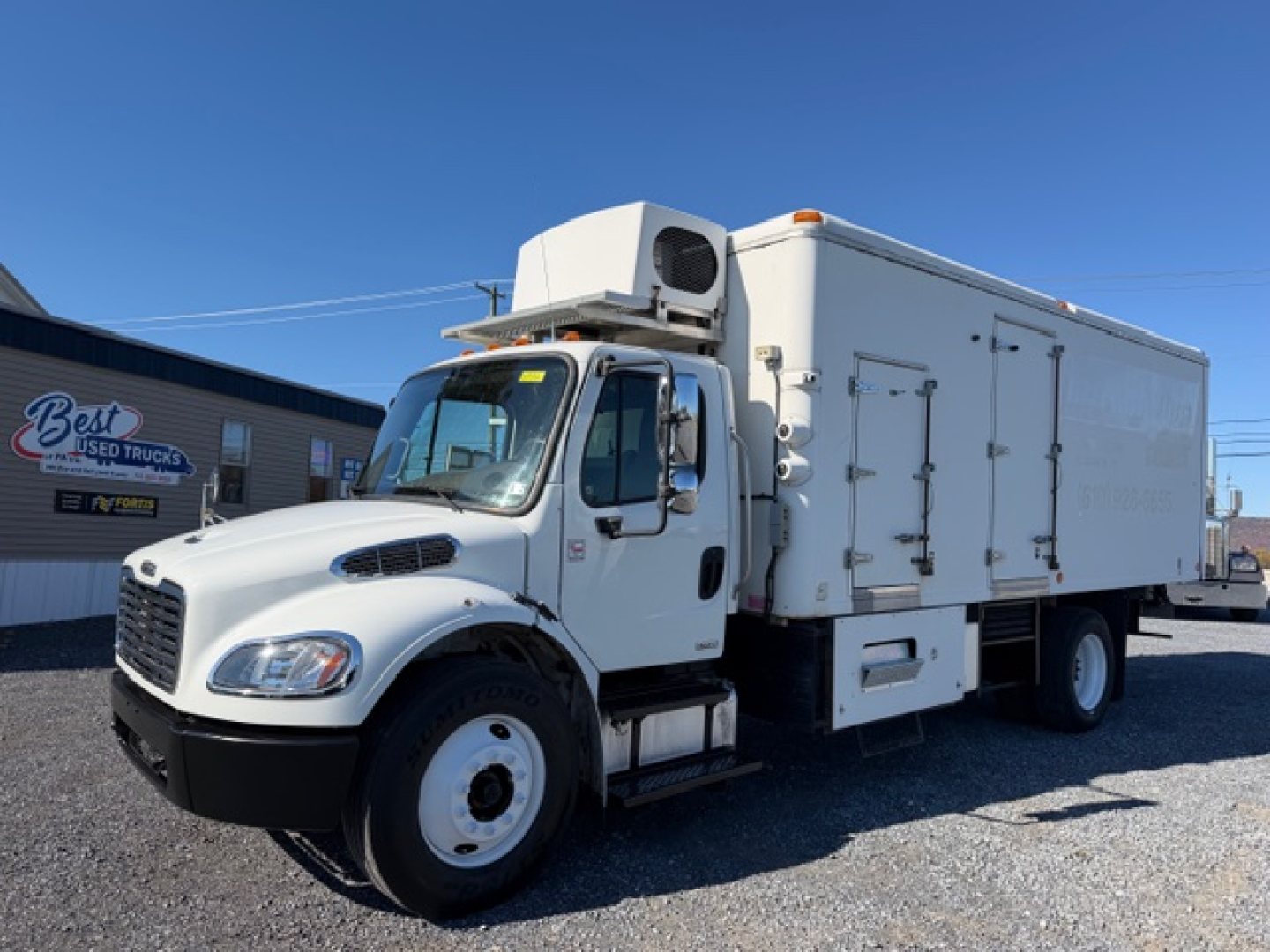 Truck in a lot showing a white Freightliner M2 106 refrigeration unit with driver cab and refrigerated box; no legible model text visible on side.
