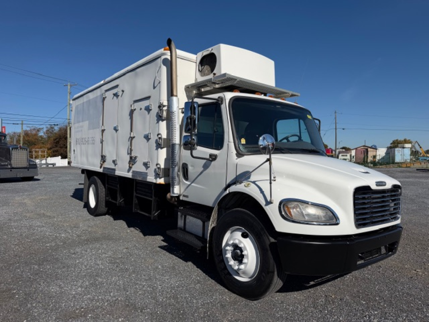 Freightliner M2 106 refrigerated truck left-front view showing cab and cargo box with white exterior and refrigeration unit on top.