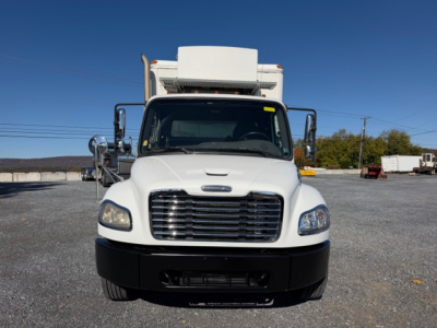 2009 Freightliner M2 106 truck front view. White cab with large grille, refrigerator unit on top, black bumper. Side mirrors extend out. Clear sky.