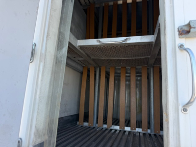 Truck interior cargo area with vertical steel slats and a grated floor hatch. Bare metal surfaces visible.