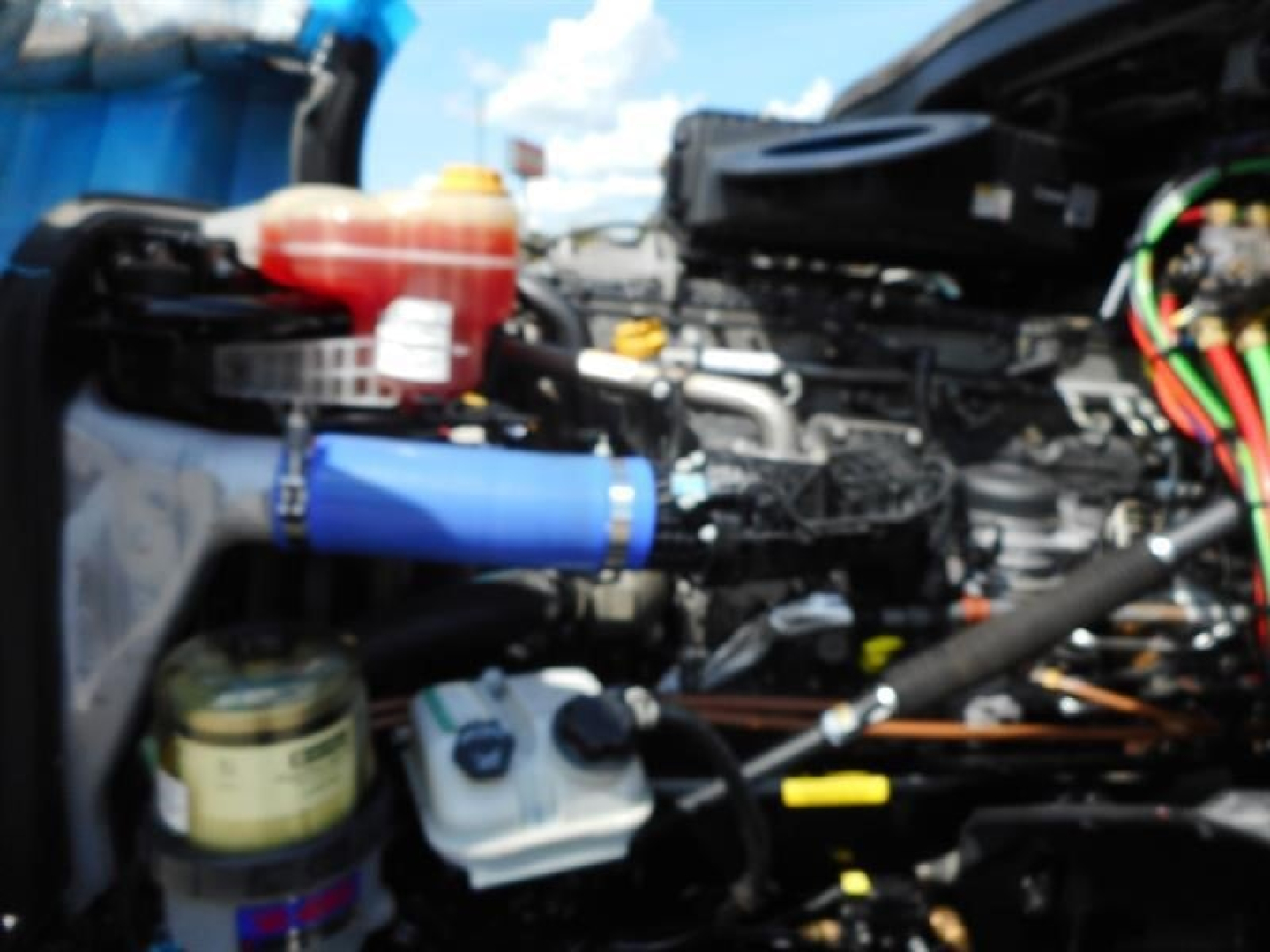 Truck engine bay of a 2023 Freightliner Cascadia 126 showing coolant reservoir, power steering fluid reservoir, and various hoses and components.