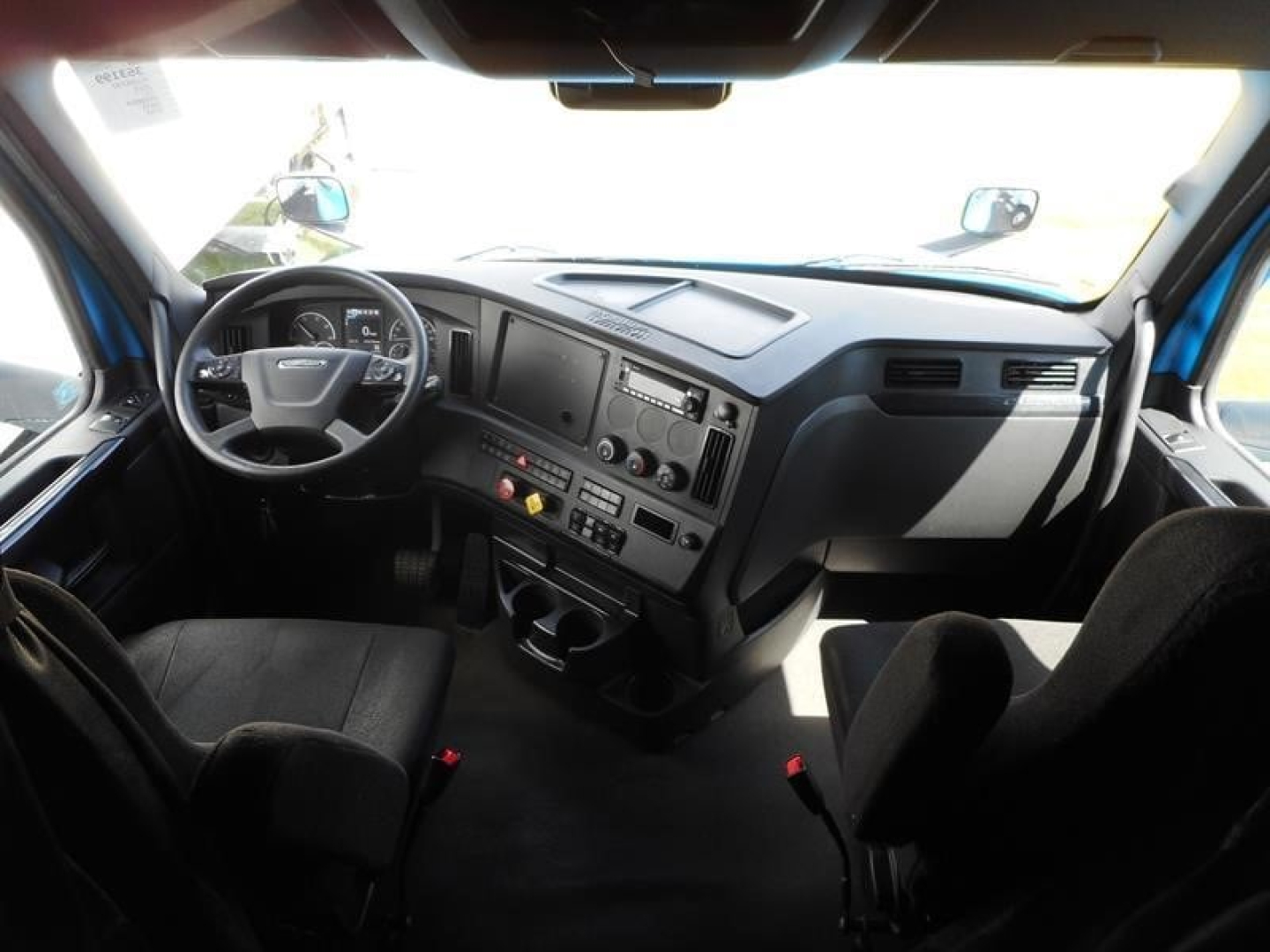 Truck cab interior showing steering wheel, dashboard with gauges, center console, and driver seat in a Freightliner Cascadia model cab.