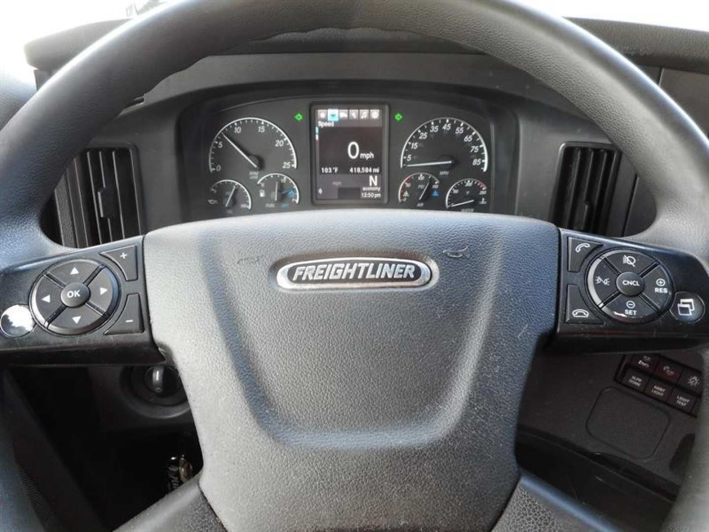 Freightliner Cascadia dashboard view through steering wheel showing instrument cluster and control buttons with Freightliner emblem on steering wheel.