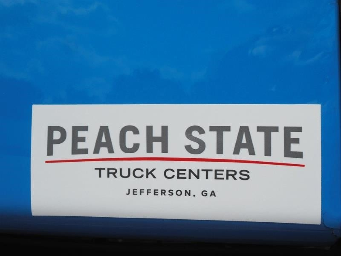 Peach State Truck Centers sticker on blue surface reading PEACH STATE TRUCK CENTERS JEFFERSON, GA