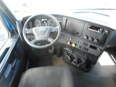 Cab interior of a Freightliner Cascadia showing steering wheel, dashboard with gauges, center console, and cupholders.