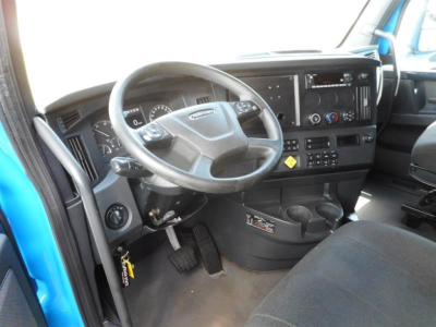 Truck cab interior showing steering wheel, dashboard, and pedals; keys hanging near ignition; center console with radio and controls.
