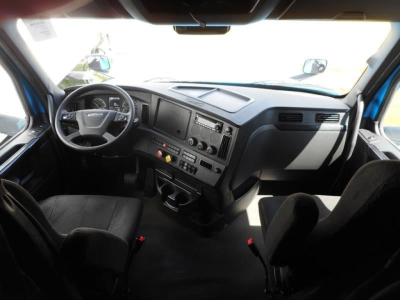 Truck cab interior showing steering wheel, dashboard with gauges, center console, and driver seat in a Freightliner Cascadia model cab.