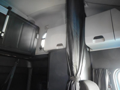 Cab interior of a Freightliner Cascadia sleeper showing upper storage cabinets and a sun visor/partition, with curtains and a window